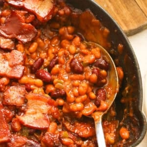 Southern Baked Beans with Bacon in a Skillet Being Spooned Out