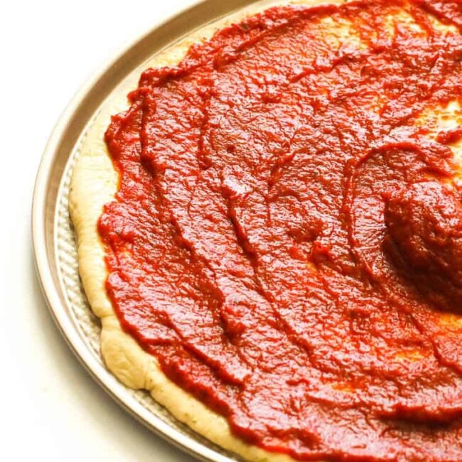 Spreading easy Homemade Pizza Sauce on a homemade pizza crust