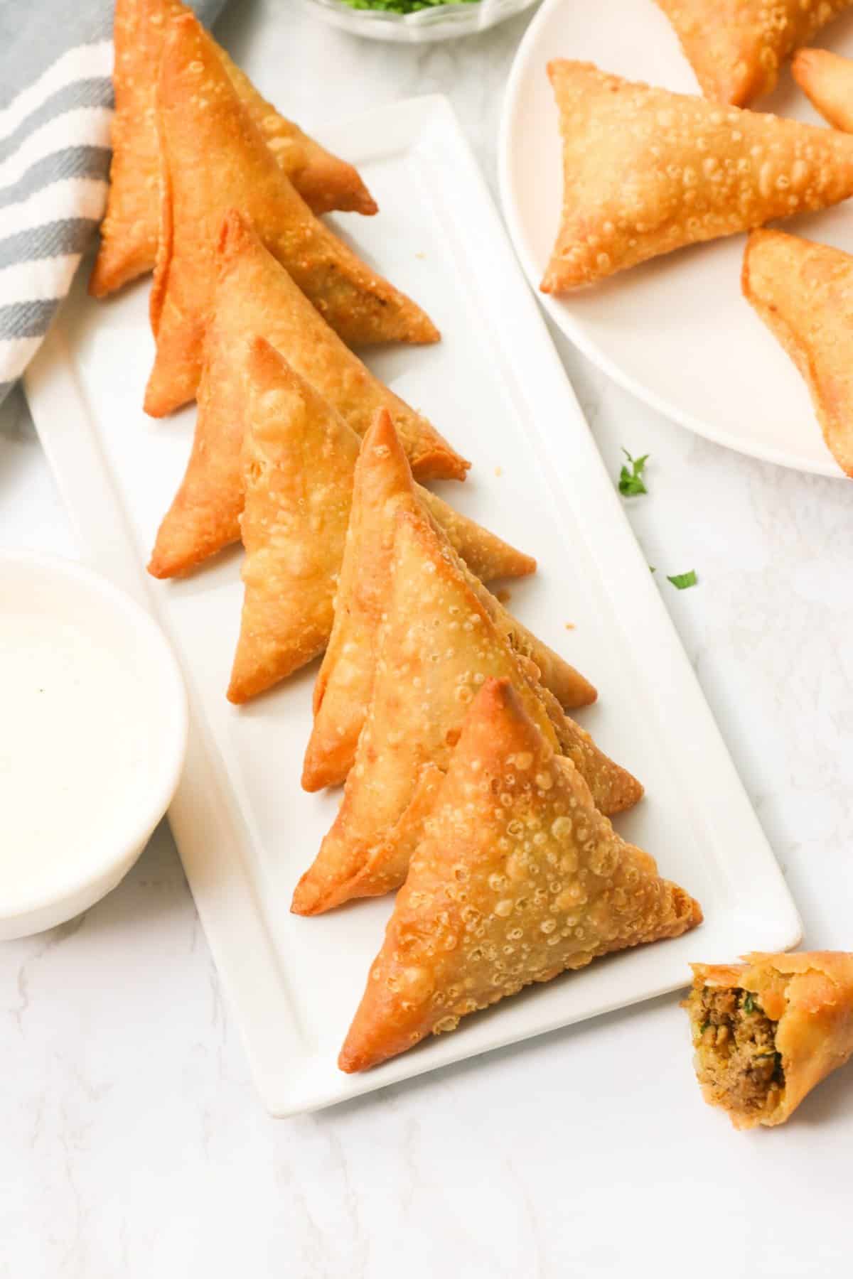 Insanely delicious sambusas stacked neatly in a row on a white rectangle plate