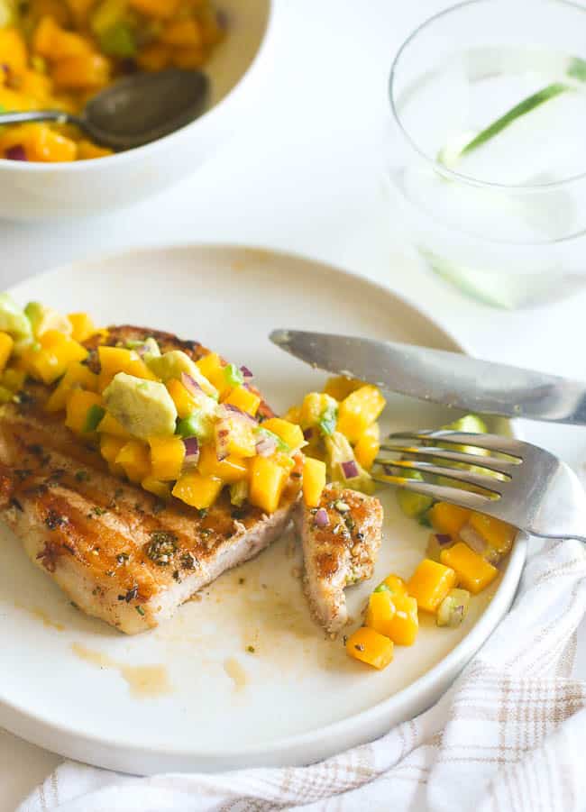 Cutting into an extra juicy marinated pork chop topped with mango salsa