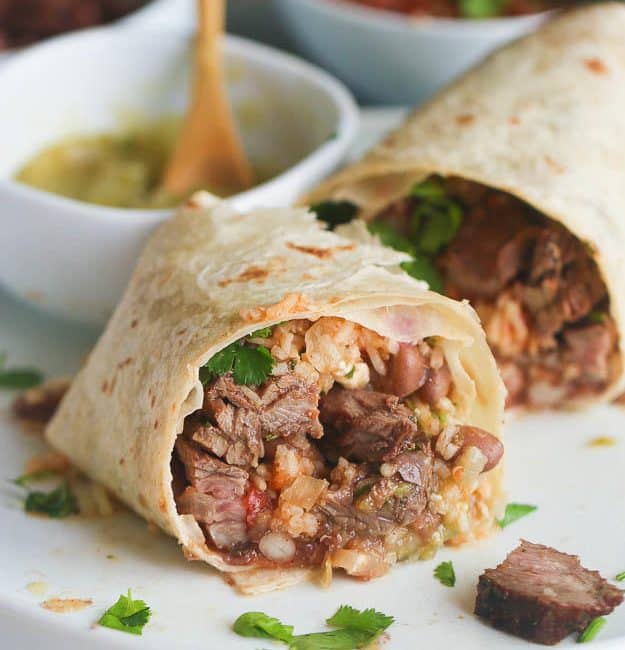 Steak Burrito sliced open for an inside view and salsa verde in the background