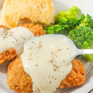 Slathering tasty white gravy over fried chicken and biscuits