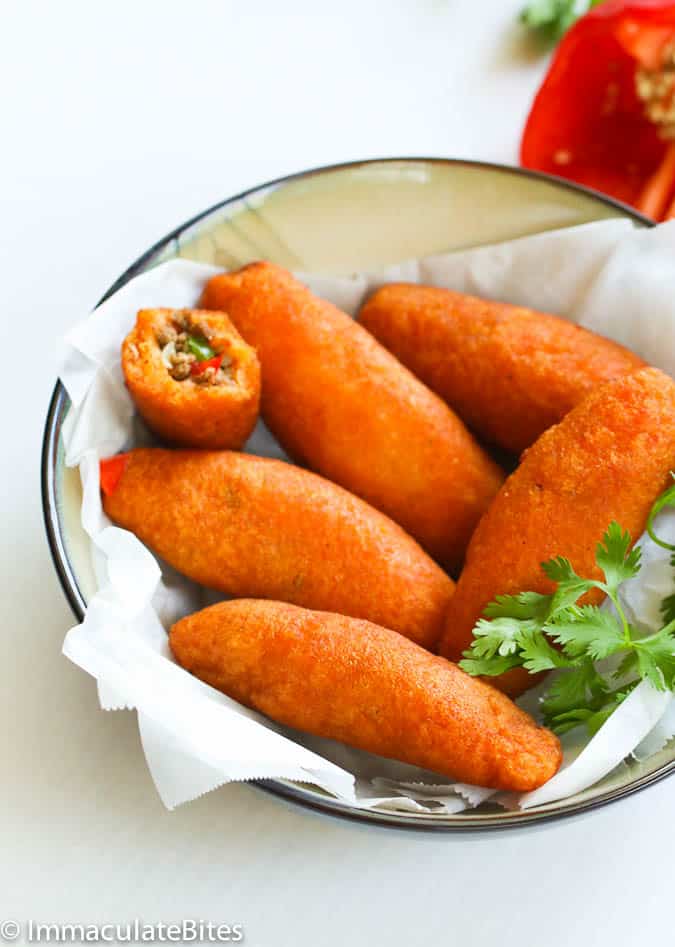 Alcapurrias in a bowl. One is missing a bite so you can see the picadillo inside