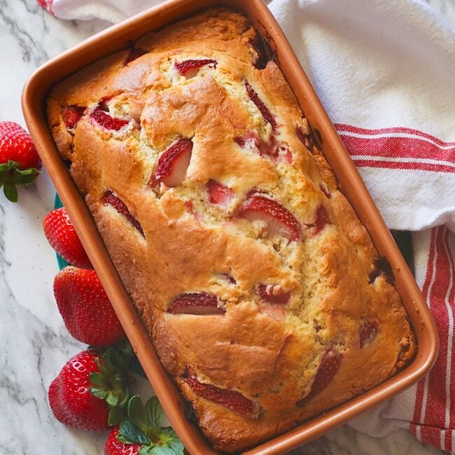 Insanely delicious freshly baked strawberry bread ready to slice with fresh strawberries on the side