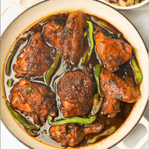 A pot of fresh brown stew chicken with Caribbean rice and beans on the side