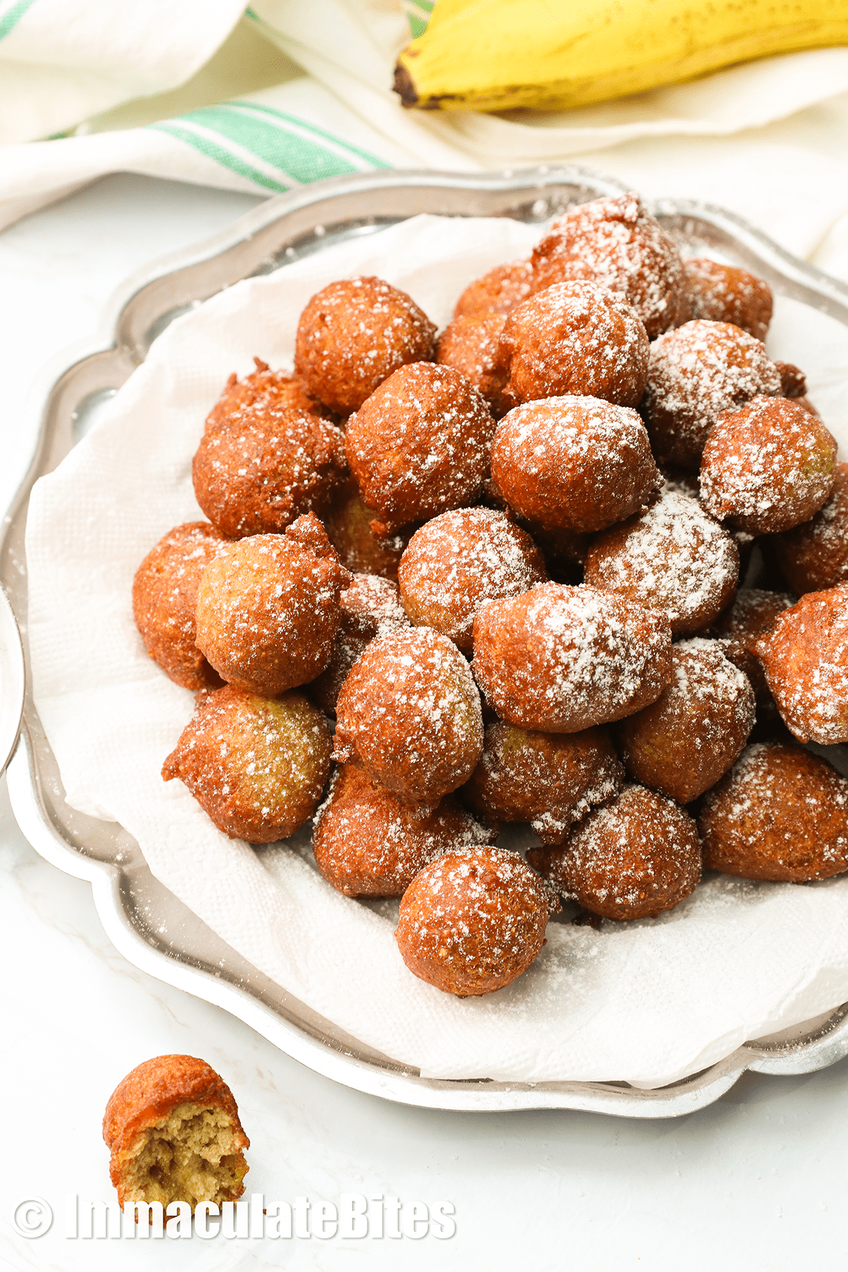 Banana fritters on a white plate with a fresh banana in the background